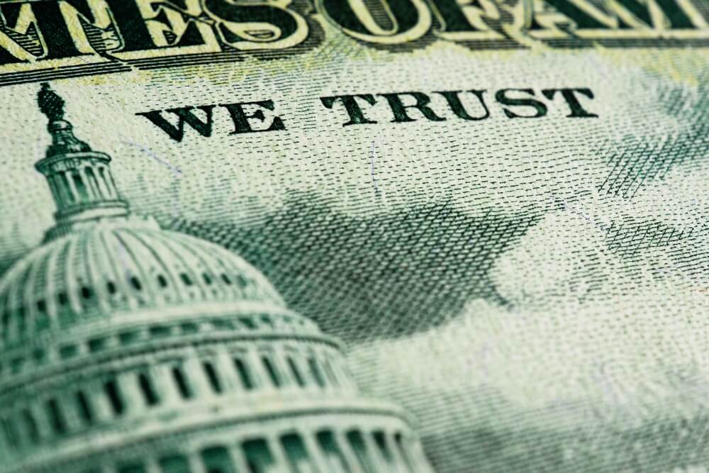 Close-up of a U.S. dollar bill featuring the Capitol building and the words 'WE TRUST', symbolizing U.S. national debt and government fiscal policy.