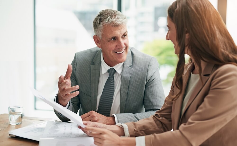 A smiling financial professional discussing wealth management documents with a client, illustrating a trusted advisory relationship.